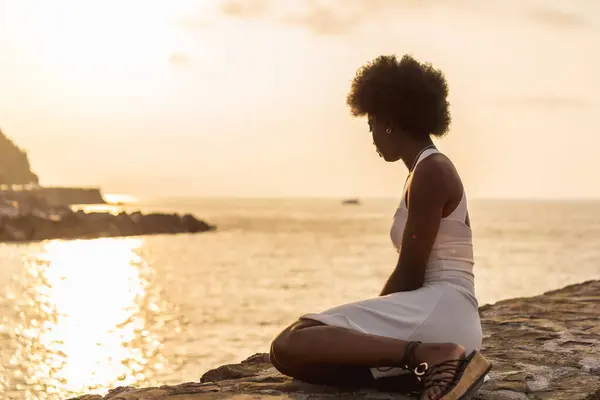 Tranquil scene of an afro woman gazing the ocean during sunset