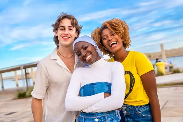 Frontal portrait of three diverse friends posing looking at camera and smiling