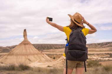 Çölde yürürken selfie çeken bir kadının arka görüntüsü.
