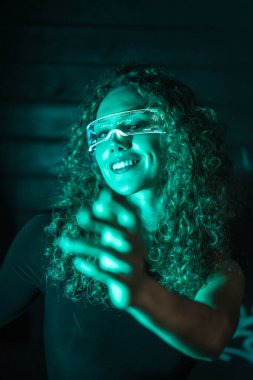 Dikey yakın plan portresi, parlak gözlükleri olan, fütürist gülümseyen genç bir kadının yeşil neon ışıkları.