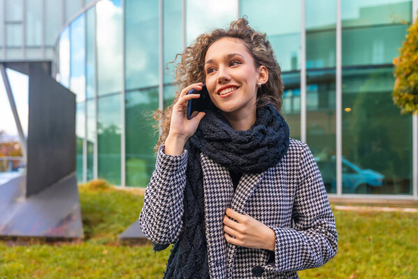 Elegant woman using phone in the city street in autumn