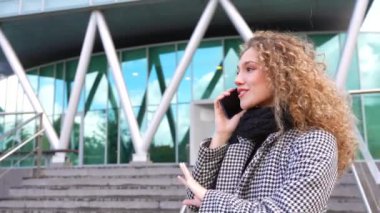 Güzel bir iş kadını, sıcak ve zarif giysiler içinde sonbaharda açık havada cep telefonuyla konuşuyor.