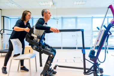 Mekanik dış iskelet. Fizyoterapi asistanı kalkmak için engelli birini robot iskeletle kaldırıyor. Modern bir hastanede gelecekteki rehabilitasyon, fizyoterapi