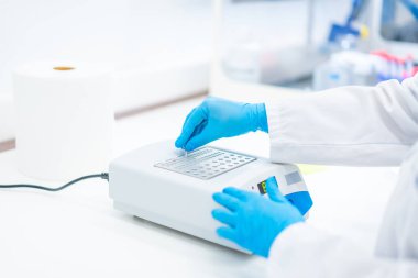 Koruyucu mavi lateks eldivenli bir biyologun elleri hücreleri analiz eden bir makine üzerinde çalışıyor.