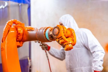 Koruyucu teçhizatlı endüstriyel boyacı endüstriyel robot endüstrisinde robotik bir kolu spreyle boyuyor.