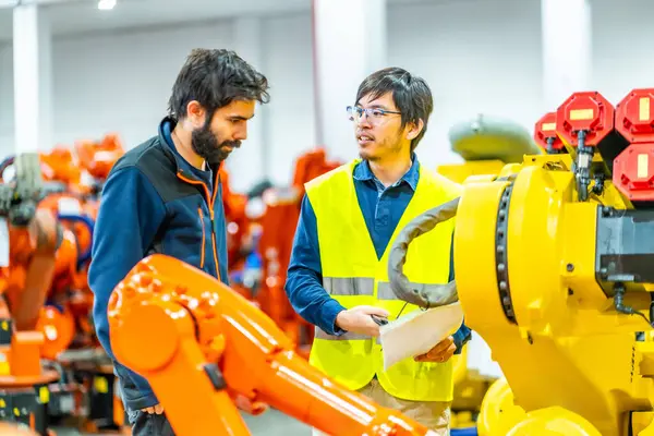 Japanese and caucasian engineers controlling the production of industrial robotic arms