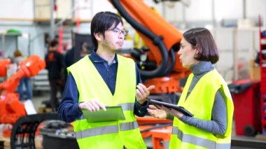 Çoklu etnik çeşitlilikte genç mühendisler, robot silah üretim hattını incelerken dikkatleri dağılmış sohbet ediyorlar.