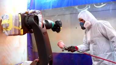 Endüstriyel ressam endüstriyel robot endüstrisinde bir robotik kolu spreyle boyuyor.