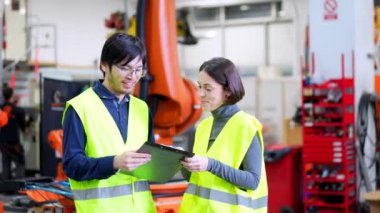 Mühendisler dijital tablet kullanarak bir robotik kol fabrikasının üretimini kontrol ediyorlar.