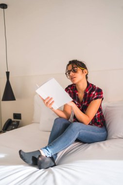Otel odasında kitap okuyan çekici genç bir kadın.