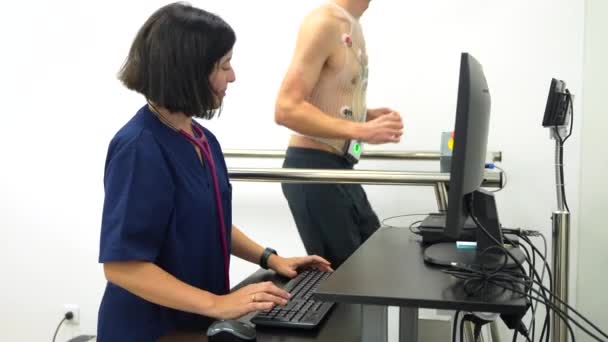 在跑步机上行走的病人正在做心血管压力测试 而一位心脏病医生在监测 — 图库视频影像