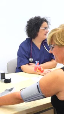 Kardiyoloji ziyareti sırasında yetişkin bir hastanın tansiyonunu ölçen hemşire.