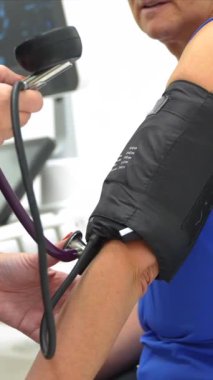 Doktor, klinikte sedyede oturan bir kadının tansiyonunu ölçüyor.