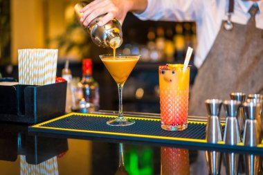 Barmen lüks bir barda martini bardağına karışık bir kokteyl dolduruyor.
