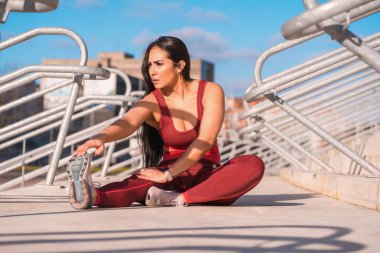 Parkta oturmuş bacağını esneten atletik bir kadının ön görüntüsü.