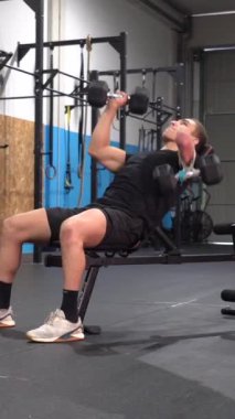 Kolu kesilmiş engelli güçlü bir adam spor salonunda dambıllarla egzersiz yapıyor.