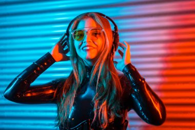 Sarışın, mutlu bir kadının portresi neon ışıklı bir şehirde kulaklık takıyor.