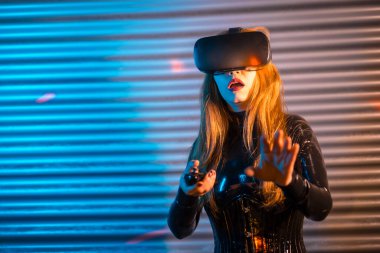 Sarışın kadın, neon ışıkları olan bir şehirde Virtutal gerçeklik gözlüğü kullanıyor.