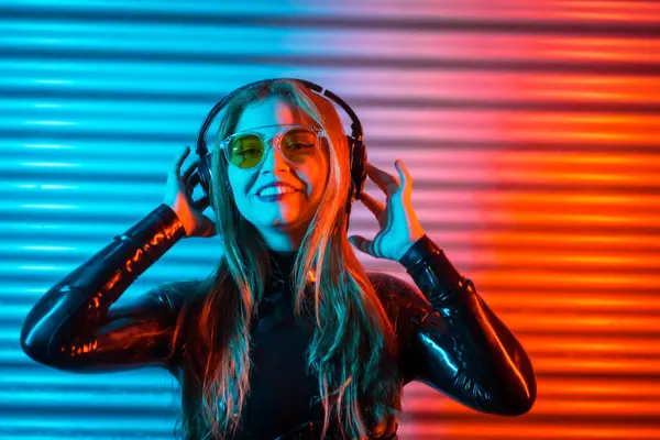 Neon ışıkları olan bir şehir kulübünde gece müzik dinlemek için kulaklık kullanan gülen kadın.