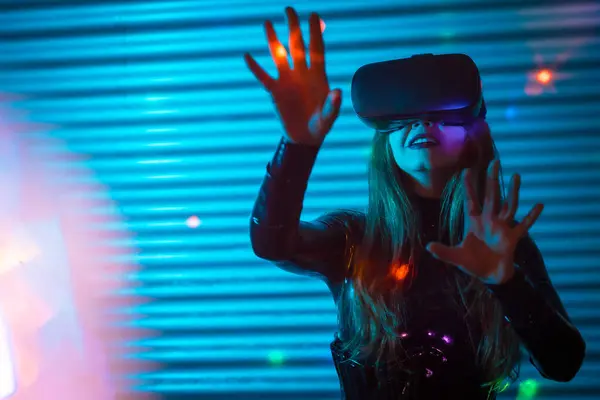 Young woman wearing augmented reality glasses touching screen with hands in an urban night space with neon lights
