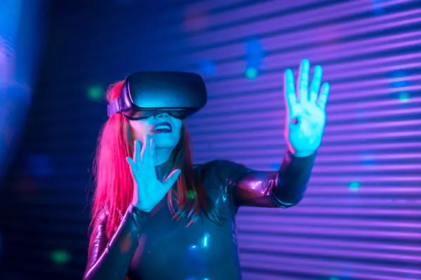 Happy woman during an interactive game with VR goggles in an urban night space with neon lights