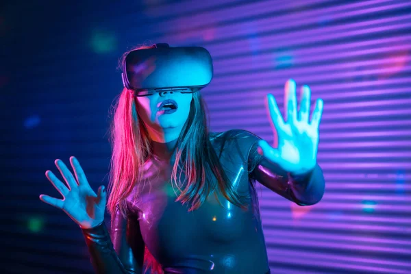 Surprised woman using augmented reality goggles in a futuristic space at night with neon lights