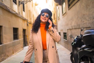 Şehirde bavul taşırken telefonla konuşan zarif Latin kadın.