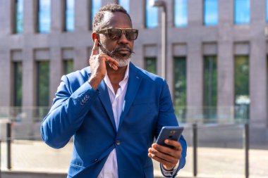 Havalı Afrikalı iş adamı kulaklığı kullanarak finans bölgesinde ayakta duran cep telefonuyla konuşuyor.