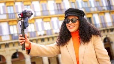 Latin tarzı bir kadın sonbaharda bir şehri ziyaret ederken kameraya el sallıyor.