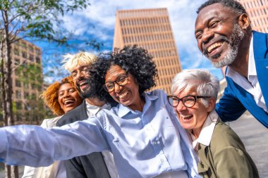 Çok ırklı iş arkadaşları gülümsüyor ve dışarıda selfie çekiyor.