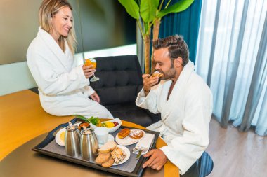 Lüks bir otel odasında bornozlu çift lezzetli bir kahvaltı yapıyor.
