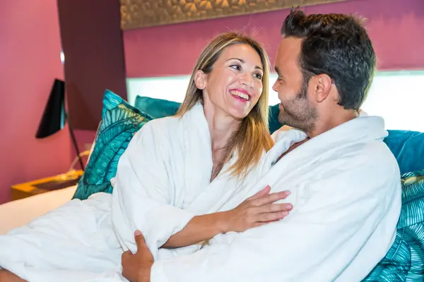 Couple dressing bathrobe embracing and relaxing in the luxury bed of an hotel