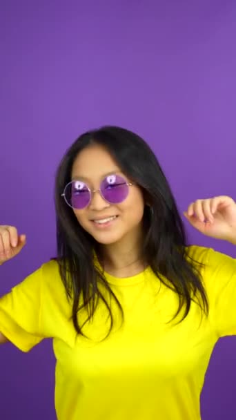 一个戴着太阳镜 带着微笑跳舞的中国女人的紫色背景的工作室照片 — 图库视频影像
