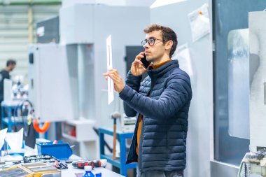 Bilgisayar sayısal kontrol fabrikasında cep telefonuyla konuşan bir mühendis.