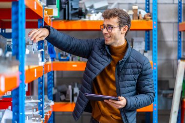 Bir fabrikanın deposunda tablet kullanan ve gülümseyen gururlu bir mühendis.