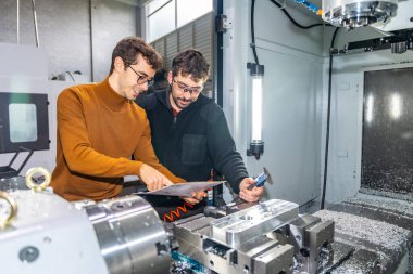 Cnc modern bir fabrikada iki erkek mühendis bir değirmen makinesinin yanında parçaları inceliyor.