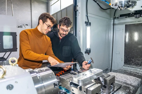 Two male engineers examining pieces next to a milling machine in a cnc modern factory