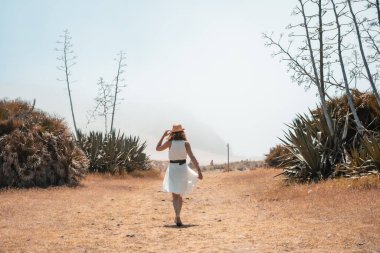 İspanya 'nın Cabo de Gata kentindeki kum tepeleri arasında yol almak için sahilin girişine doğru yürüyen bir kadın.