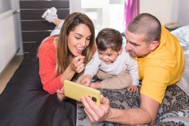 Mutlu bir aile yatakta uzanmış selfie çekiyor.