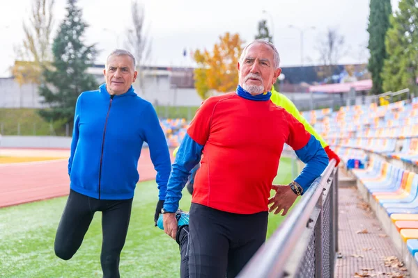 Old people stretching together before running in an outdoor track in a venue in winter
