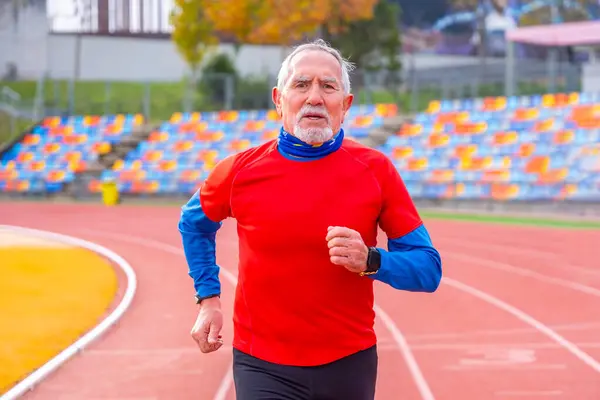 Frontal view portrait of an old man doing en effort running in an athletic track