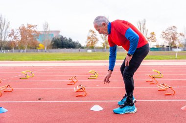 Sportif son sınıf öğrencisi koni yerleştiriyor ve kışın açık havada antrenman yapmak için atletizm pistine başlangıç blokları koyuyor.
