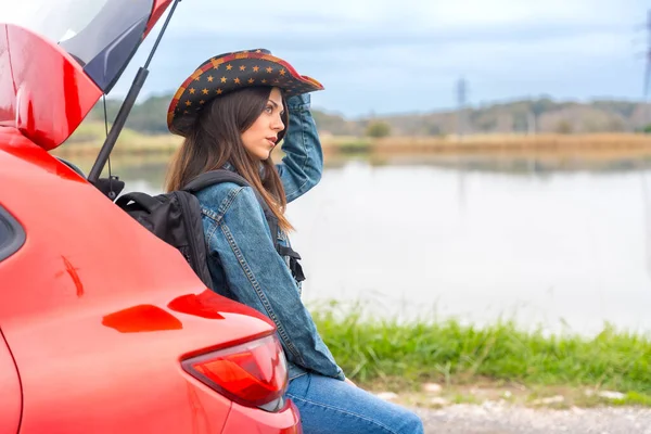 Side view of a solo traveler relaxing during a road trip with a red car