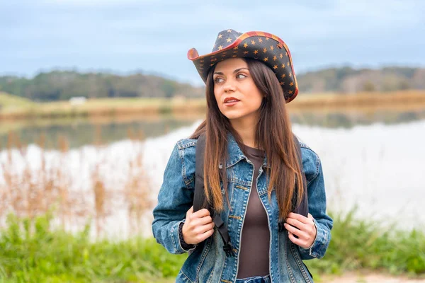 Portrait of a beauty female explorer with denim clothes, bag and hat next to a lake