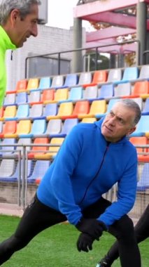 Kışın atletizm pistinde gerinen üç yetişkin adam.