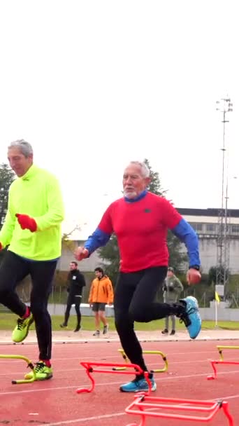 Sportlicher Senior Platziert Kegel Und Startblöcke Auf Leichtathletikbahn Für Training — Stockvideo