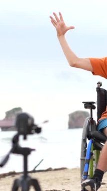 Tekerlekli sandalyedeki engelli birinin portresi plajda bir video kaydediyor.