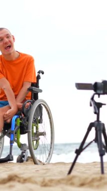 Tekerlekli sandalyede sakat birinin portresi plajın yanında video kaydediyor.