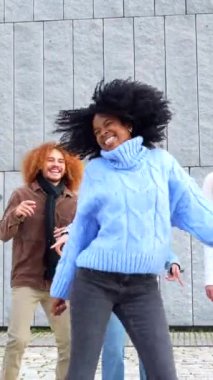 Sokakta çok ırklı arkadaşların arasında dans eden bir kadın kol kaldırıyor.
