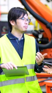 Çoklu etnik çeşitlilikte genç mühendisler, robot silah üretim hattını incelerken dikkatleri dağılmış sohbet ediyorlar.